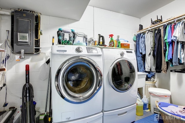 clothes washing area featuring electric panel, concrete block wall, laundry area, and washer and clothes dryer