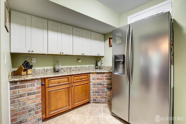 kitchen with stainless steel fridge, light tile patterned flooring, brown cabinetry, white cabinets, and light stone countertops