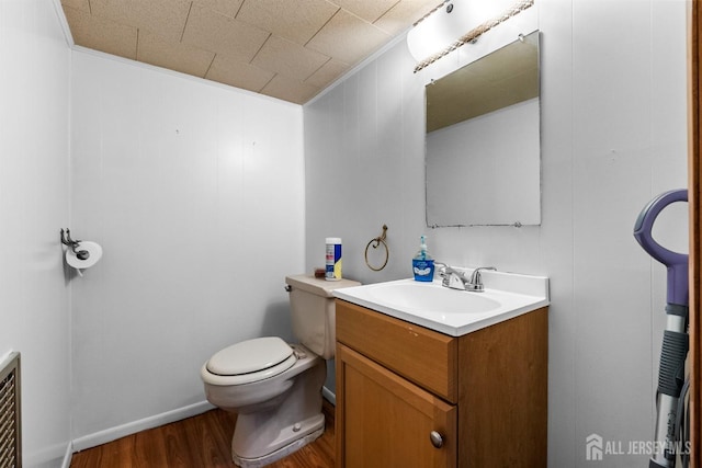 half bathroom with vanity, ornamental molding, wood finished floors, and toilet