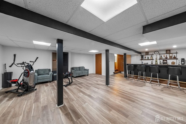 workout room featuring light wood-style flooring, a paneled ceiling, and bar