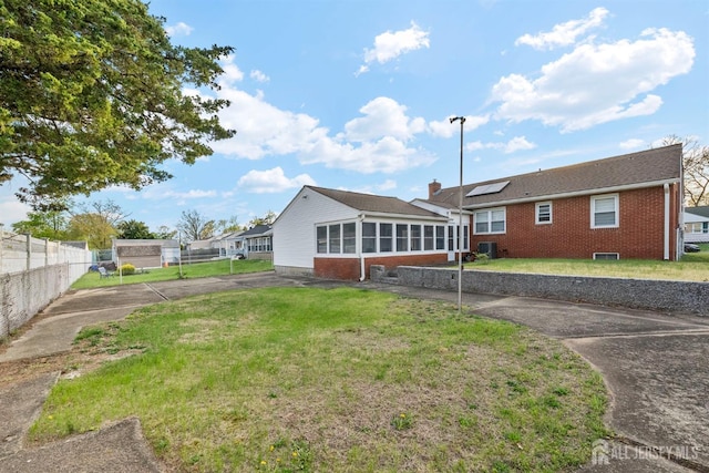 back of house with a yard, brick siding, fence, and a sunroom