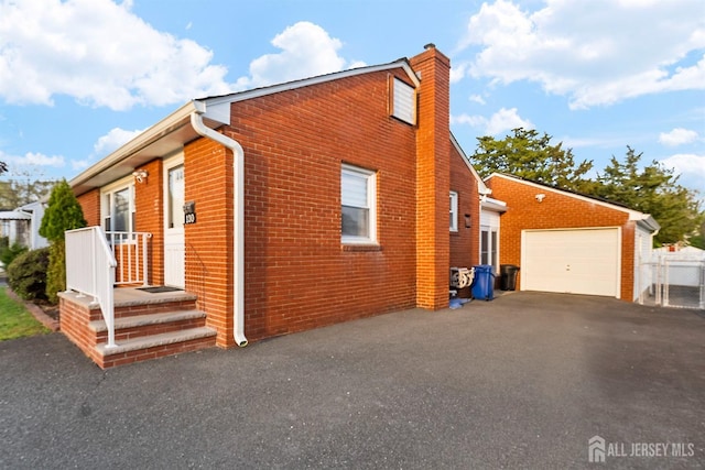 view of side of property featuring brick siding, driveway, a chimney, and a garage