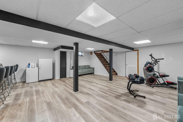 finished basement with freestanding refrigerator, stairs, wood finished floors, fridge, and a drop ceiling