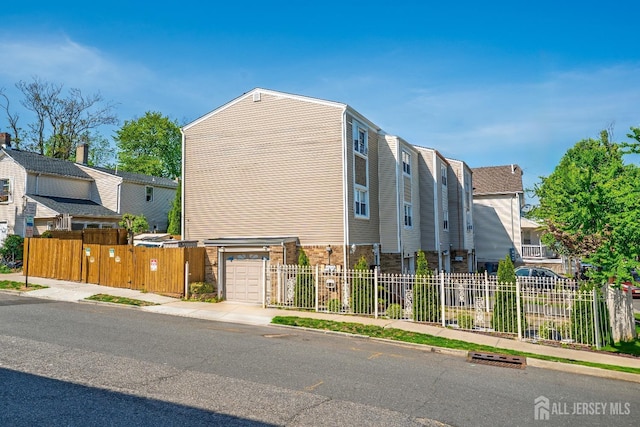 view of front of home with a garage, fence, concrete driveway, and a residential view
