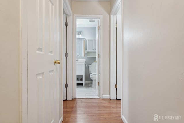 hall featuring baseboards, visible vents, and light wood-style floors