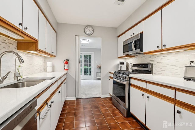 kitchen with appliances with stainless steel finishes, a sink, white cabinetry, and light countertops