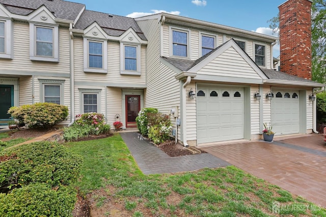 townhome / multi-family property with decorative driveway, an attached garage, and roof with shingles