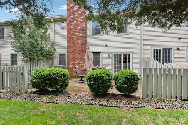 rear view of property featuring a chimney, fence, and a patio area