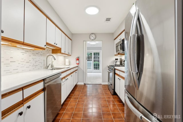 kitchen featuring appliances with stainless steel finishes, a sink, tasteful backsplash, light countertops, and white cabinets