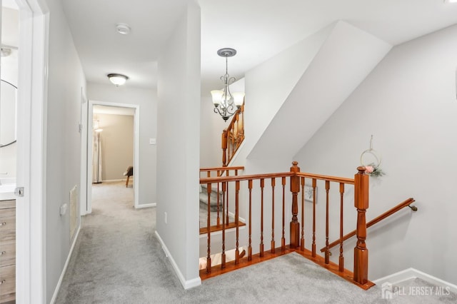 corridor with an upstairs landing, carpet flooring, baseboards, and a chandelier