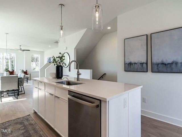 kitchen with a kitchen island with sink, a sink, stainless steel dishwasher, dark wood-style flooring, and hanging light fixtures