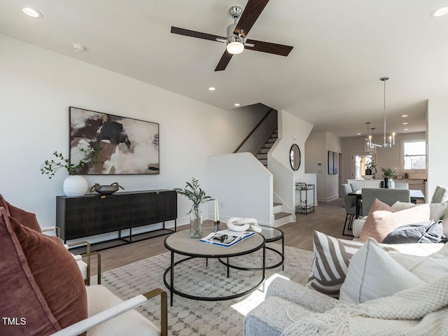 living room featuring ceiling fan with notable chandelier, wood finished floors, recessed lighting, baseboards, and stairs