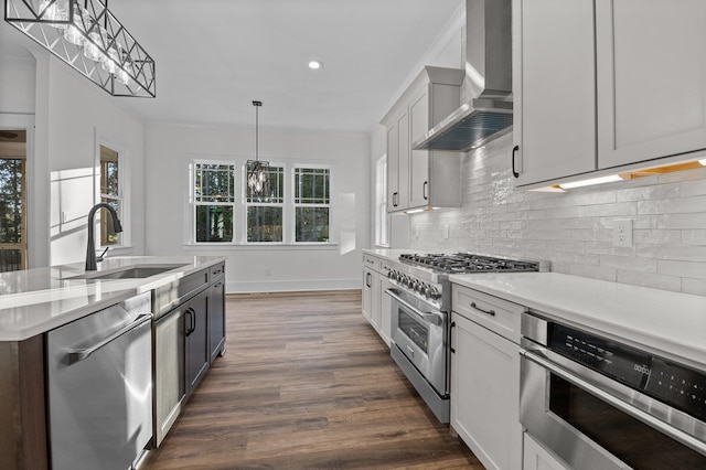 kitchen with wall chimney range hood, sink, hanging light fixtures, dark hardwood / wood-style flooring, and stainless steel appliances