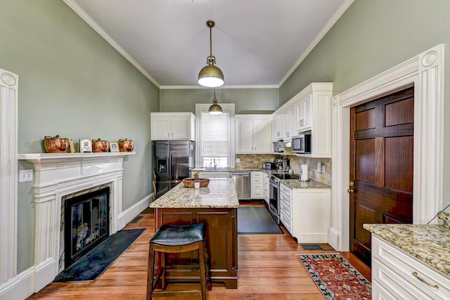 kitchen featuring light stone counters, a kitchen island, hanging light fixtures, stainless steel appliances, and light wood-type flooring