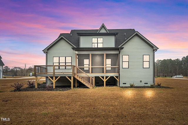 back house at dusk with a wooden deck and a lawn