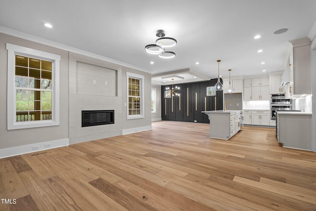 interior space featuring ornamental molding, decorative light fixtures, white cabinetry, and light hardwood / wood-style flooring