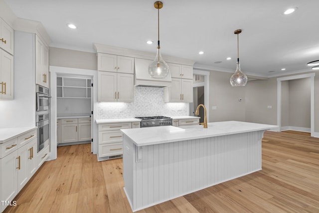 kitchen with appliances with stainless steel finishes, decorative light fixtures, light wood-type flooring, and white cabinetry