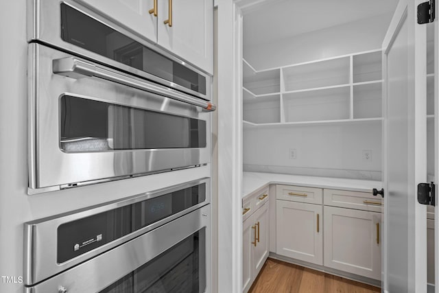 kitchen with white cabinetry, stainless steel double oven, and light wood-type flooring