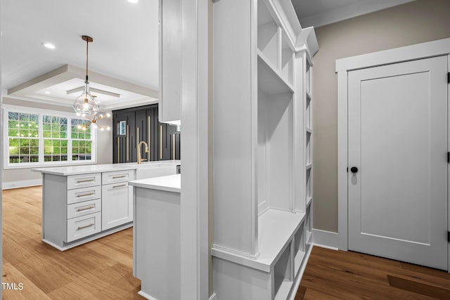 mudroom featuring an inviting chandelier, light wood-type flooring, a raised ceiling, and sink