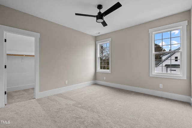 unfurnished bedroom featuring light carpet, a walk in closet, a closet, and ceiling fan