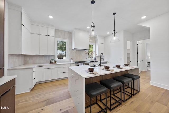 kitchen with a breakfast bar, a kitchen island with sink, white cabinets, decorative light fixtures, and light wood-type flooring