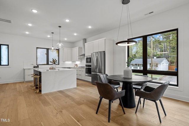 kitchen with stainless steel appliances, a kitchen island, wall chimney range hood, decorative light fixtures, and white cabinetry