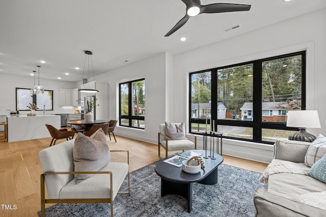 living room with ceiling fan with notable chandelier and light wood-type flooring