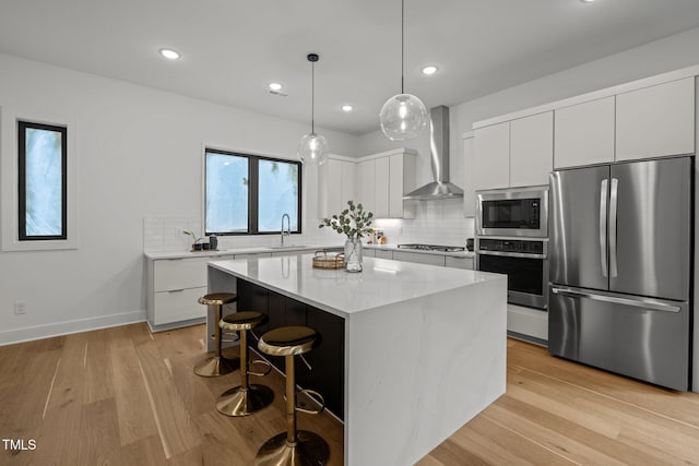 kitchen with a center island, white cabinets, wall chimney range hood, sink, and appliances with stainless steel finishes