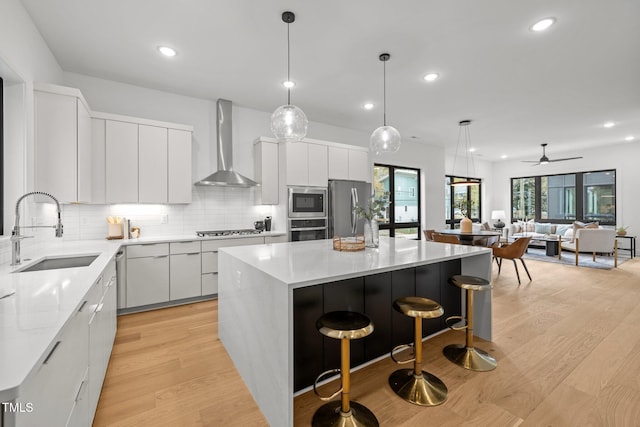 kitchen with appliances with stainless steel finishes, wall chimney exhaust hood, sink, white cabinets, and a kitchen island