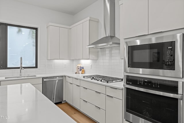 kitchen featuring sink, wall chimney range hood, backsplash, white cabinets, and appliances with stainless steel finishes