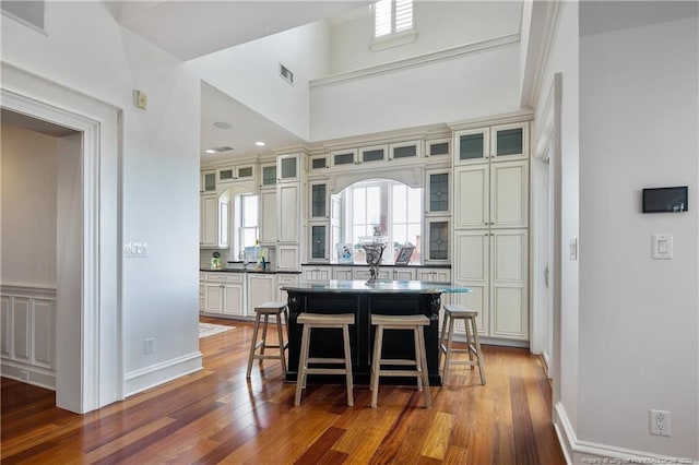 kitchen featuring hardwood / wood-style floors, a kitchen island, a high ceiling, and a kitchen breakfast bar