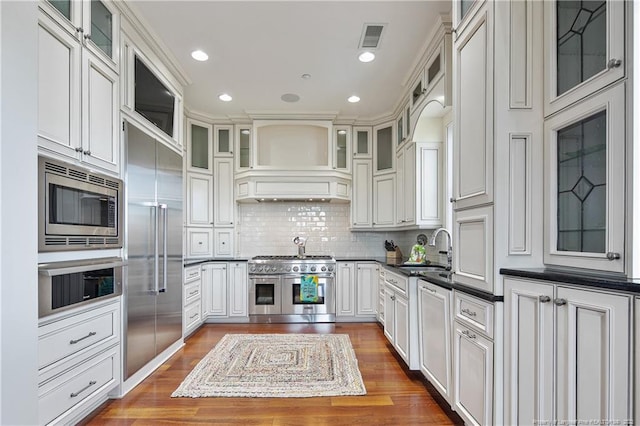 kitchen with dark hardwood / wood-style flooring, sink, decorative backsplash, white cabinets, and built in appliances