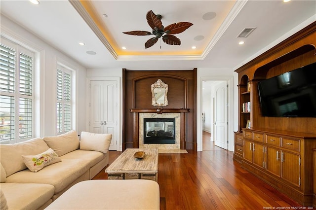 living room with a raised ceiling, dark hardwood / wood-style floors, a high end fireplace, and ceiling fan