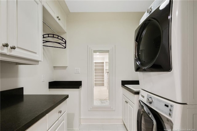 kitchen with stacked washer and clothes dryer, light tile patterned floors, and white cabinetry