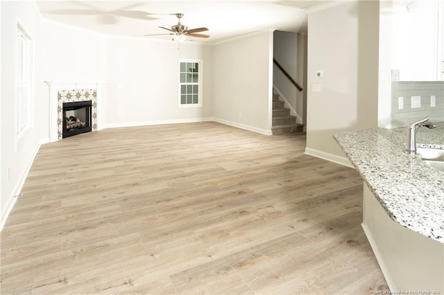 living room with crown molding, ceiling fan, sink, and light wood-type flooring