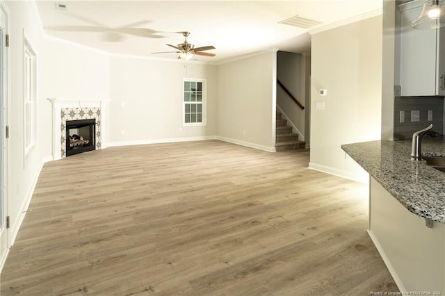 living room featuring light wood-type flooring, ornamental molding, sink, a tile fireplace, and ceiling fan