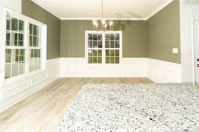 empty room with a notable chandelier, light wood-type flooring, and ornamental molding