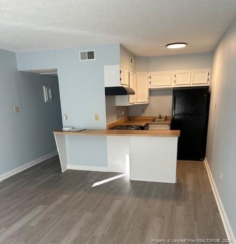 kitchen featuring kitchen peninsula, dark wood-type flooring, black refrigerator, sink, and white cabinets