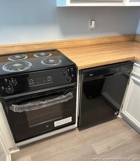 exterior space with black dishwasher, light hardwood / wood-style flooring, range, and white cabinets