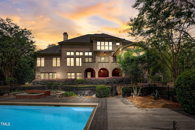 back house at dusk featuring a swimming pool with hot tub