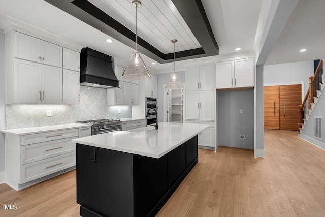 kitchen with light wood-type flooring, premium range hood, a tray ceiling, and white cabinets