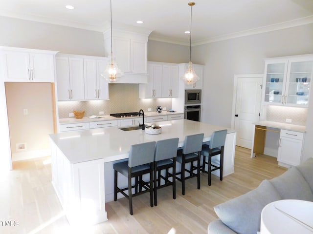 kitchen with white cabinetry, decorative light fixtures, stainless steel appliances, and an island with sink