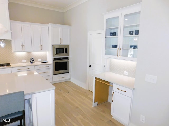 kitchen with appliances with stainless steel finishes, white cabinets, decorative backsplash, ornamental molding, and light wood-type flooring