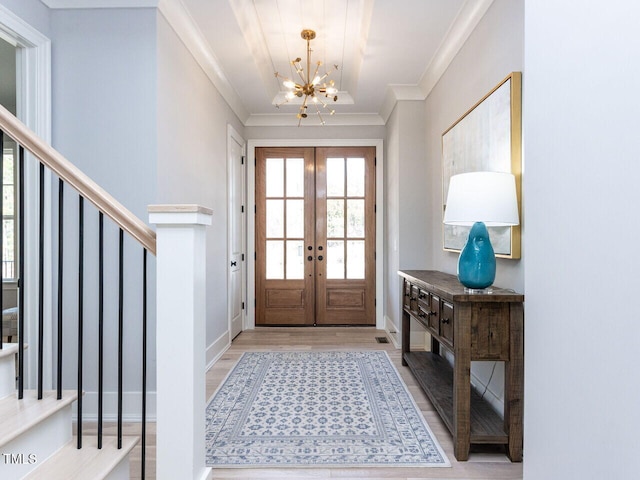 entrance foyer with french doors, a notable chandelier, crown molding, light wood finished floors, and stairs