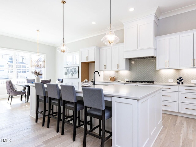 kitchen featuring a center island with sink, white cabinets, ornamental molding, light countertops, and pendant lighting