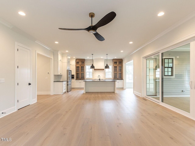 kitchen featuring light wood-type flooring, sink, decorative light fixtures, a center island with sink, and white cabinets