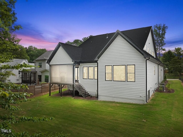 back house at dusk with a yard and a sunroom