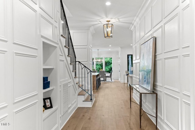 foyer entrance featuring ornamental molding, light wood-type flooring, and a notable chandelier