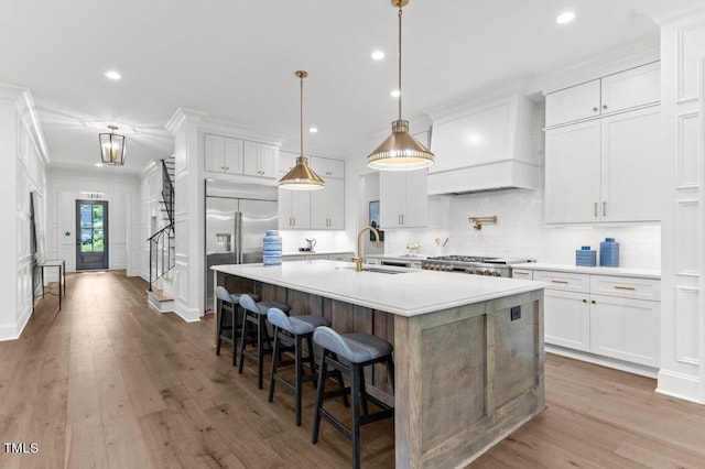 kitchen featuring stainless steel appliances, an island with sink, wood-type flooring, white cabinets, and custom range hood