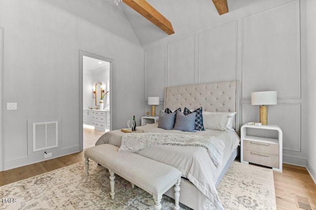 bedroom featuring lofted ceiling with beams, light wood-type flooring, ensuite bathroom, and ceiling fan